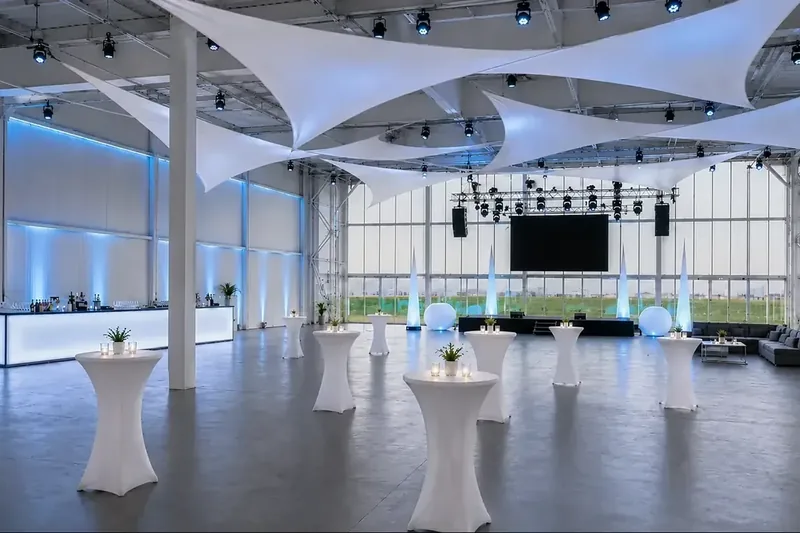 Hell und festlich eingedeckter Hangar mit Lichtsegeln und großen Tafeln bei aircraft events